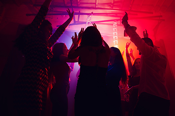 Image showing A crowd of people in silhouette raises their hands against colorful neon light on party background