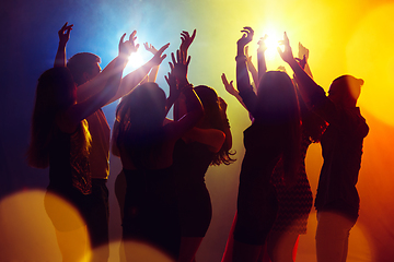 Image showing A crowd of people in silhouette raises their hands against colorful neon light on party background