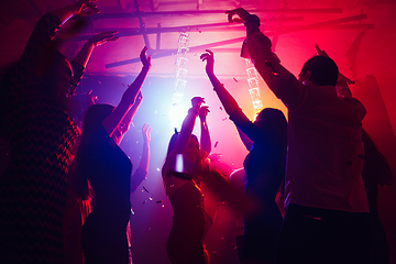 Image showing A crowd of people in silhouette raises their hands against colorful neon light on party background