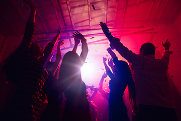 Image showing A crowd of people in silhouette raises their hands against colorful neon light on party background