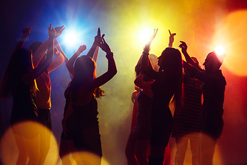 Image showing A crowd of people in silhouette raises their hands against colorful neon light on party background