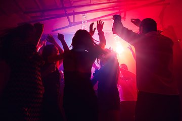 Image showing A crowd of people in silhouette raises their hands against colorful neon light on party background