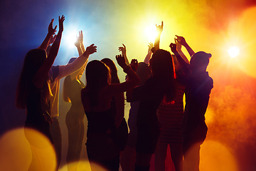 Image showing A crowd of people in silhouette raises their hands against colorful neon light on party background