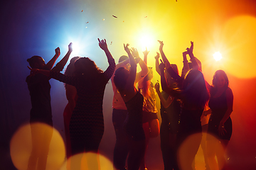Image showing A crowd of people in silhouette raises their hands against colorful neon light on party background