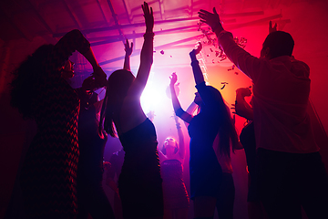 Image showing A crowd of people in silhouette raises their hands against colorful neon light on party background