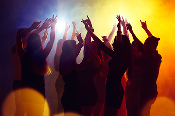 Image showing A crowd of people in silhouette raises their hands against colorful neon light on party background