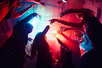 Image showing A crowd of people in silhouette raises their hands against colorful neon light on party background