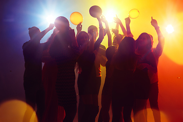 Image showing A crowd of people in silhouette raises their hands against colorful neon light on party background