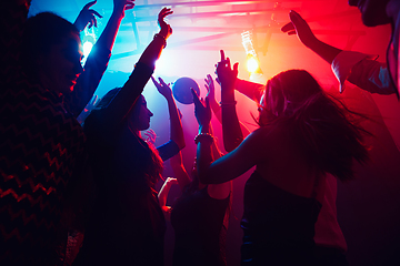 Image showing A crowd of people in silhouette raises their hands against colorful neon light on party background