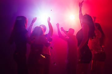 Image showing A crowd of people in silhouette raises their hands against colorful neon light on party background