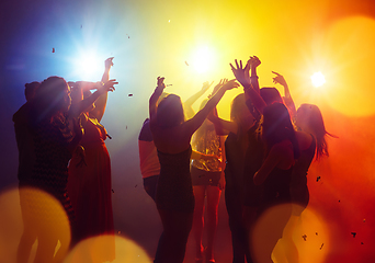 Image showing A crowd of people in silhouette raises their hands against colorful neon light on party background