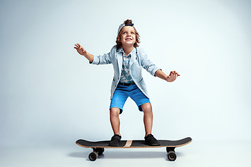 Image showing Pretty young boy on skateboard in casual clothes on white studio background