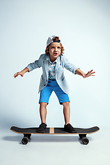 Image showing Pretty young boy on skateboard in casual clothes on white studio background