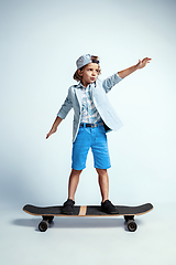 Image showing Pretty young boy on skateboard in casual clothes on white studio background