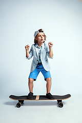 Image showing Pretty young boy on skateboard in casual clothes on white studio background