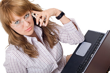 Image showing The young woman in glasses sits with the laptop and phone. Isola