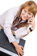 Image showing The smiling young woman sits with the laptop and phone. Isolated