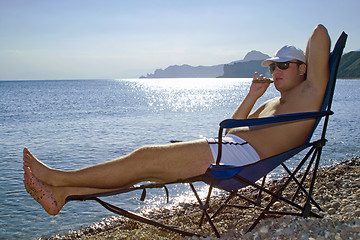 Image showing The young man with a cigar has a rest on seacoast