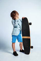 Image showing Pretty young boy on skateboard in casual clothes on white studio background