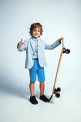 Image showing Pretty young boy on skateboard in casual clothes on white studio background