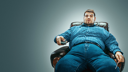 Image showing Fat man sitting in a brown armchair, emotional watching TV