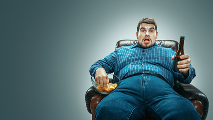 Image showing Fat man sitting in a brown armchair, emotional watching TV