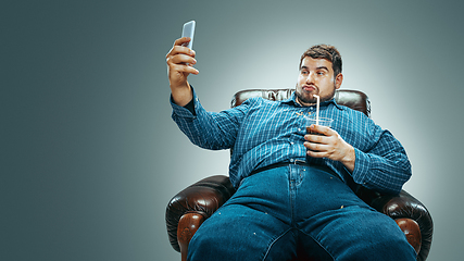 Image showing Fat man sitting in a brown armchair, emotional watching TV