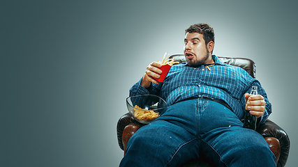 Image showing Fat man sitting in a brown armchair, emotional watching TV