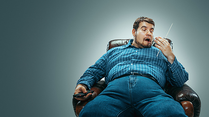 Image showing Fat man sitting in a brown armchair, emotional watching TV