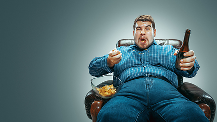 Image showing Fat man sitting in a brown armchair, emotional watching TV