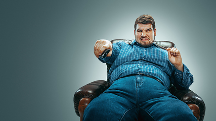 Image showing Fat man sitting in a brown armchair, emotional watching TV