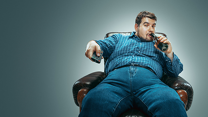 Image showing Fat man sitting in a brown armchair, emotional watching TV