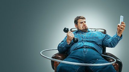 Image showing Fat man sitting in a brown armchair, emotional watching TV