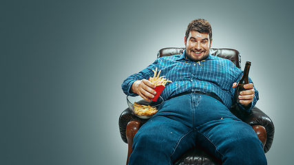 Image showing Fat man sitting in a brown armchair, emotional watching TV