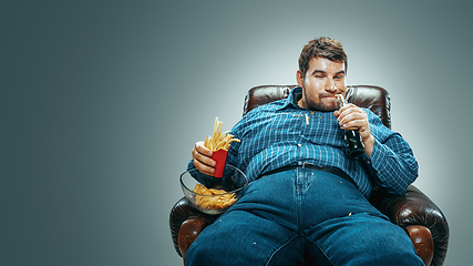 Image showing Fat man sitting in a brown armchair, emotional watching TV