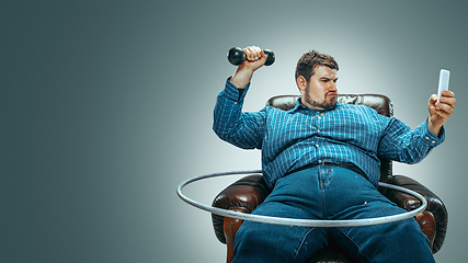 Image showing Fat man sitting in a brown armchair, emotional watching TV