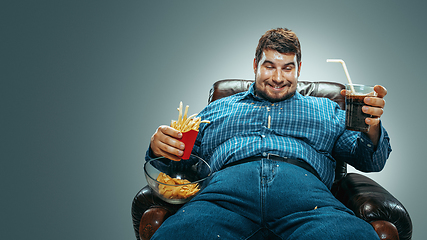 Image showing Fat man sitting in a brown armchair, emotional watching TV