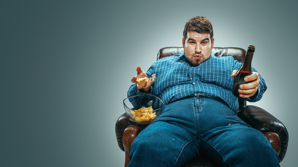 Image showing Fat man sitting in a brown armchair, emotional watching TV