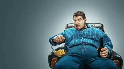 Image showing Fat man sitting in a brown armchair, emotional watching TV