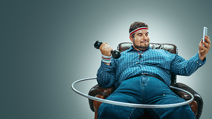 Image showing Fat man sitting in a brown armchair, emotional watching TV