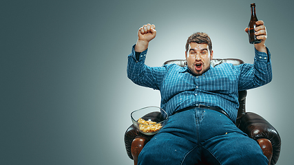 Image showing Fat man sitting in a brown armchair, emotional watching TV