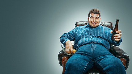 Image showing Fat man sitting in a brown armchair, emotional watching TV