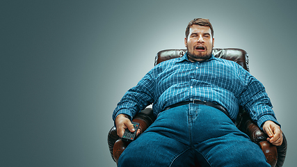 Image showing Fat man sitting in a brown armchair, emotional watching TV