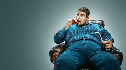 Image showing Fat man sitting in a brown armchair, emotional watching TV