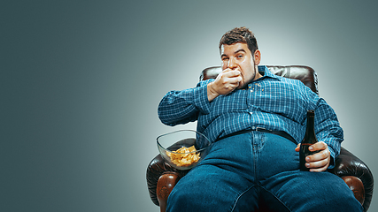 Image showing Fat man sitting in a brown armchair, emotional watching TV