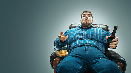 Image showing Fat man sitting in a brown armchair, emotional watching TV