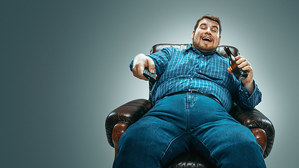 Image showing Fat man sitting in a brown armchair, emotional watching TV