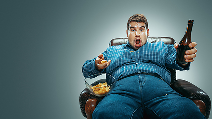 Image showing Fat man sitting in a brown armchair, emotional watching TV