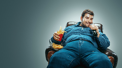 Image showing Fat man sitting in a brown armchair, emotional watching TV