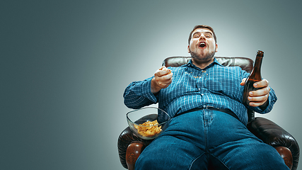 Image showing Fat man sitting in a brown armchair, emotional watching TV